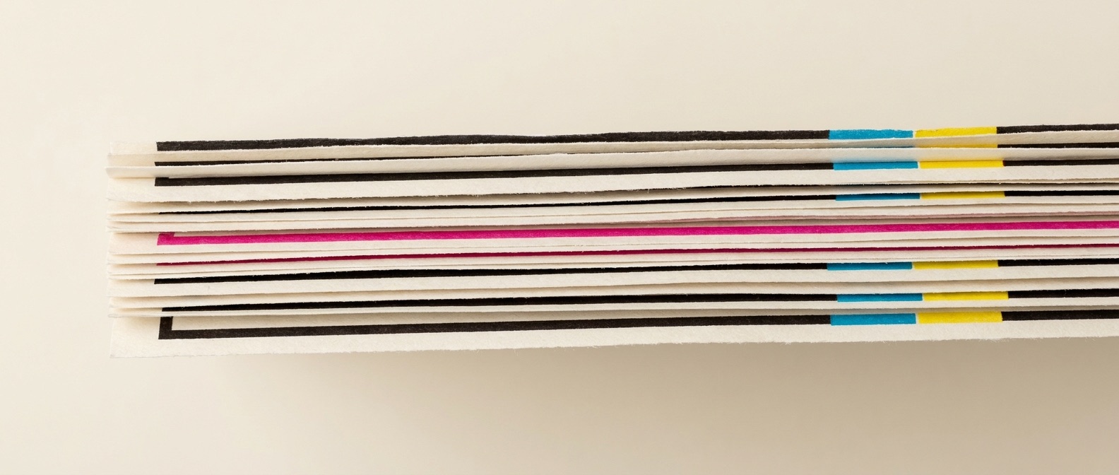 Overlapping paper proof sheets layered like a stack of prints, ink and magenta edges visible